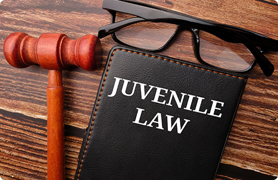 A wooden gavel next to a Juvenile Law book and glasses on a wooden desk.