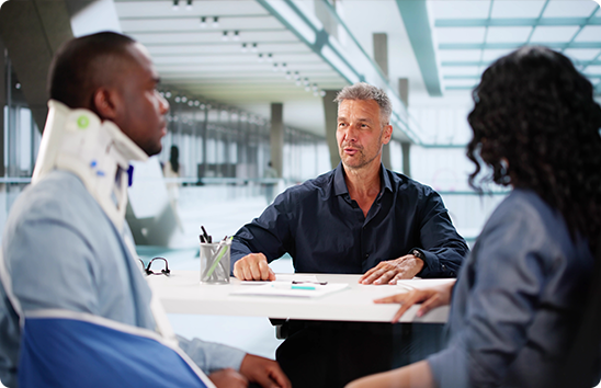 Injured man in a neck brace and arm sling consulting with an attorney about a personal injury claim.