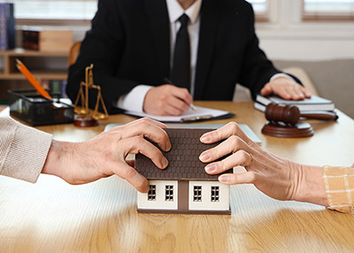 Two sets of hands pulling on a model house during a legal dispute.