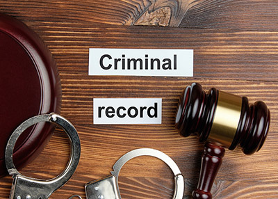 A judge's gavel, handcuffs, and a 'Criminal record' sign on a wooden desk.